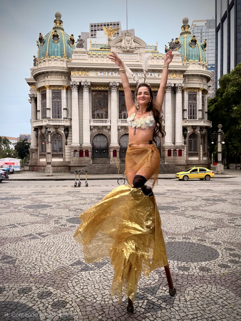 Juliane sobre pernas de pau em frente ao Theatro Municipal